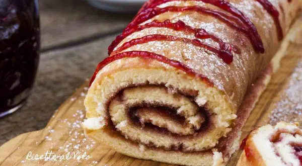 Un delizioso rotolo alla marmellata, spolverato di zucchero a velo e decorato con un filo di confettura rossa, pronto per essere gustato.