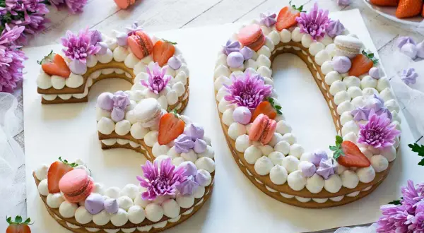 Una torta numero 30 decorata con panna, fragole, macarons e fiori viola.