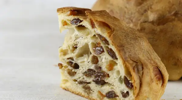 Fetta di pandolce genovese ricetta originale, con uvetta e canditi, su sfondo chiaro.