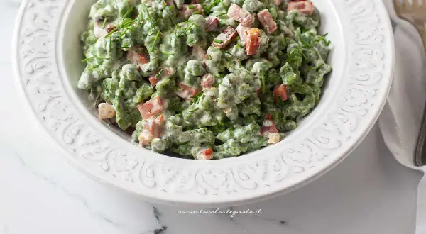 Un piatto di gnocchetti tirolesi verdi, conditi con panna, piselli e speck croccante, guarniti con erba cipollina.