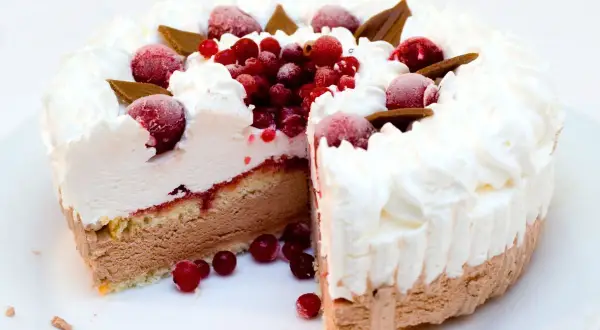 Torta gelato a strati con panna montata, frutti rossi e cioccolato. Una fetta è stata tagliata, rivelando il suo interno goloso.