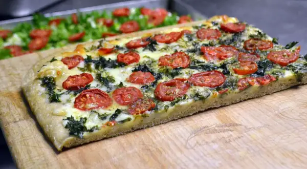 Focaccia messinese con pomodorini e verdure, un sapore autentico su un tagliere di legno.