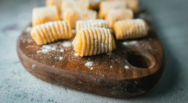 Gnocchi fatti in casa, pronti per essere cucinati. La gnocchi ricetta perfetta è a portata di mano, con questi morbidi e invitanti gnocchi su un tagliere di legno.