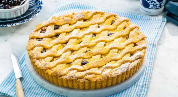 Una deliziosa crostata amalfitana con una griglia dorata di pasta frolla, cosparsa di zucchero a velo e ripiena di amarene.