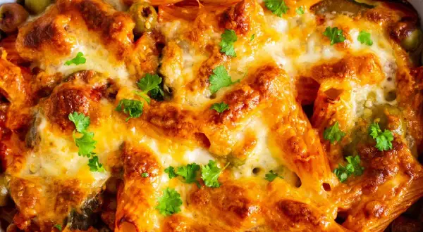 Un invitante pasta al forno ricetta della nonna, dorata e filante, con olive e prezzemolo fresco.