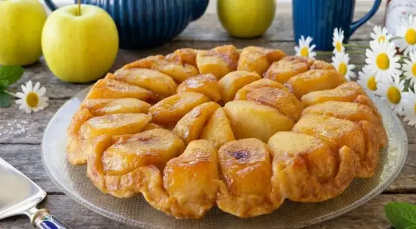Una deliziosa tarte tatin di mele dorate, con mele fresche, una teiera blu e fiori di campo.