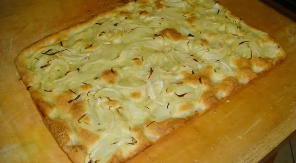 Focaccia con cipolle appena sfornata, dorata e fragrante, adagiata su un tagliere di legno.