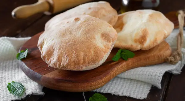 Tre soffici pane arabo dorati su un tagliere di legno, guarniti con foglie di menta fresca.