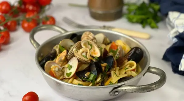 Un piatto di scialatielli ai frutti di mare, con cozze, vongole e pomodorini, guarnito con prezzemolo fresco.
