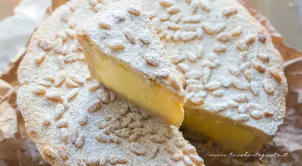 Una fetta di torta della nonna, cosparsa di pinoli e zucchero a velo, mostra il suo ripieno cremoso.