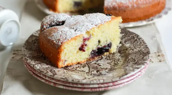 Una fetta di torta nua soffice, cosparsa di zucchero a velo, con un cuore di marmellata di frutti di bosco.