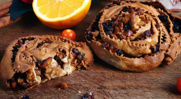 Due pitte nchiuse calabresi, dolci tradizionali con uvetta e noci, su un tagliere di legno con arancia e pomodorini.