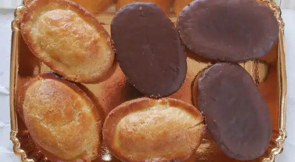 Sei fruttoni leccesi, tre ricoperti di cioccolato fondente e tre dorati, disposti su un vassoio dorato.