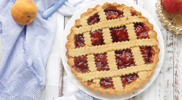 Deliziosa crostata di pesche con ripieno rosso brillante, decorata con strisce di pasta frolla a zig-zag.