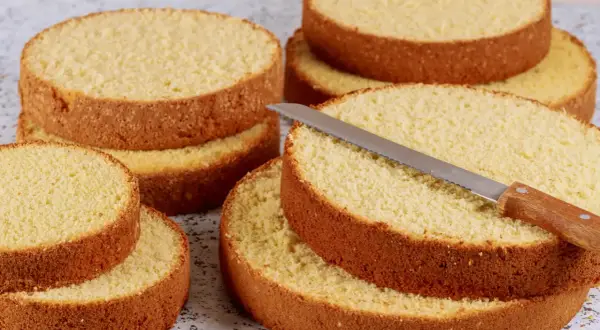 Dischi di pan di spagna dorati e soffici, pronti per essere farciti. Un coltello da torta è appoggiato su uno strato.
