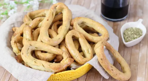 Taralli al finocchietto con lievito, croccanti e profumati, in un cestino con un bicchiere di vino rosso e semi di finocchio.