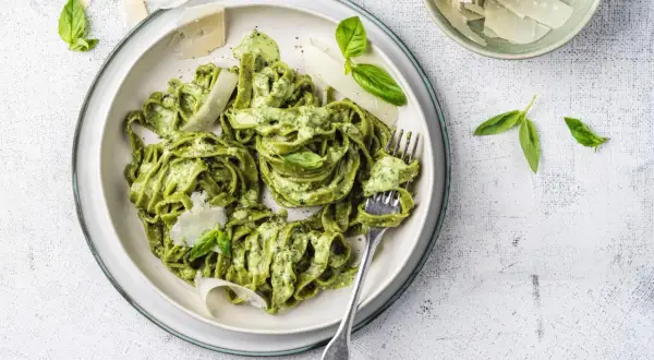 Un piatto di pasta al pesto, condita con una cremosa salsa verde, guarnita con scaglie di parmigiano e foglie di basilico fresco.