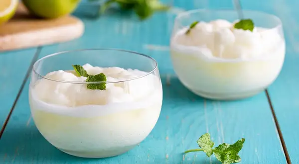 Due bicchieri di sorbetto al limone, guarniti con menta fresca, su un tavolo di legno blu.