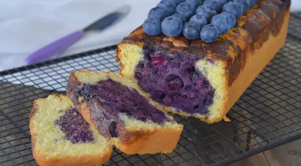 Plumcake ai mirtilli appena sfornato, con mirtilli freschi in cima e all'interno, su una griglia di raffreddamento.