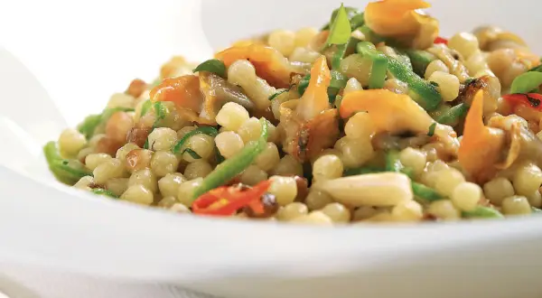 Un piatto di fregola sarda con vongole, peperoncino e zucchine, un sapore di mare e terra.