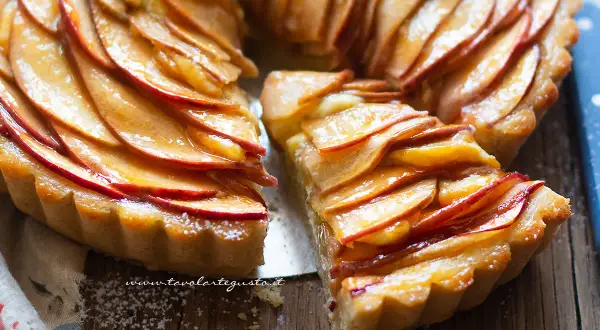 Una deliziosa crostata di mele, con fette di mela lucide disposte a spirale su una base dorata. Una fetta è stata tolta, rivelando la morbidezza.