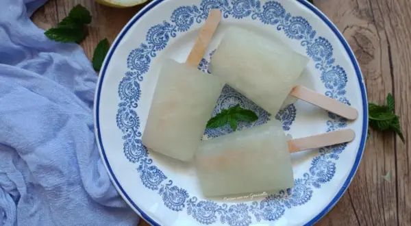 Tre ghiaccioli al limone fatti in casa su un piatto decorato, con limone e menta fresca. Perfetti per un'estate rinfrescante.