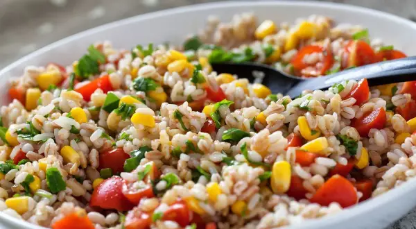 Insalata di farro colorata con pomodorini, mais e prezzemolo fresco, servita in una ciotola bianca.