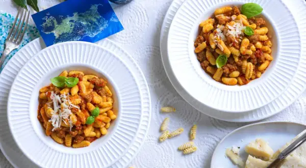 Due piatti di malloreddus alla campidanese, pasta sarda con sugo di salsiccia e pomodoro, guarniti con basilico e parmigiano.