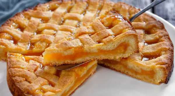 Deliziosa crostata senza glutine con ripieno di albicocche, una fetta sollevata da un coltello.