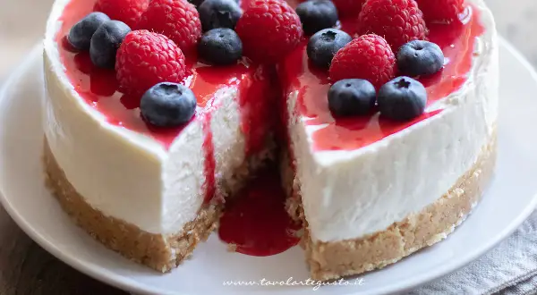 Delizioso cheesecake con mascarpone, guarnito con lamponi freschi, mirtilli e una colata di salsa rossa.