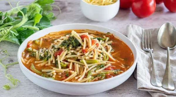Piatto di pasta con i tenerumi asciutta, pomodoro e verdure fresche, pronto per essere gustato.