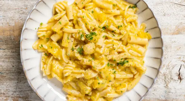 Piatto di pasta e zucca cremosa, guarnita con prezzemolo tritato e pepe nero, servita su un piatto bianco con bordo decorato.