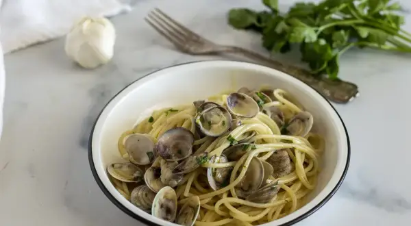 Un piatto invitante di spaghetti con le vongole, conditi con prezzemolo fresco e serviti in una ciotola bianca.