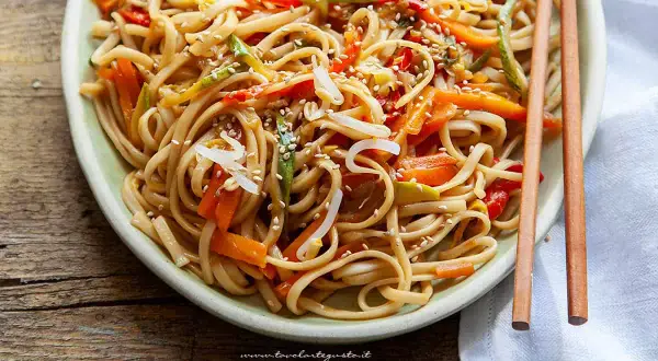 Un piatto invitante di spaghetti di riso saltati con verdure colorate e semi di sesamo, pronti per essere gustati con le bacchette.