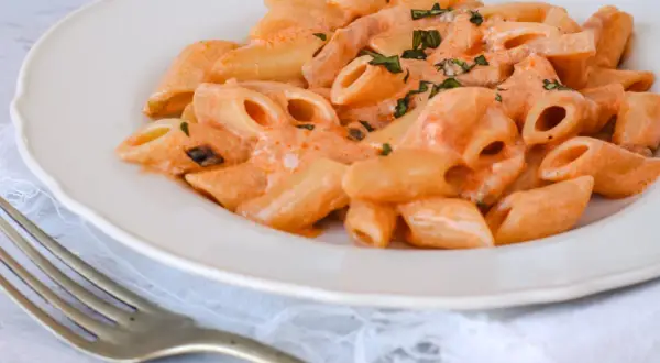 Piatto di penne alla vodka cremose, guarnite con erbe fresche, pronte per essere gustate con una forchetta.
