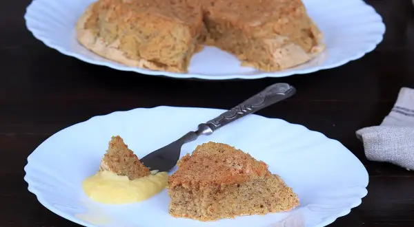 Una fetta di torta nocciole piemontese originale, soffice e dorata, servita con crema gialla.