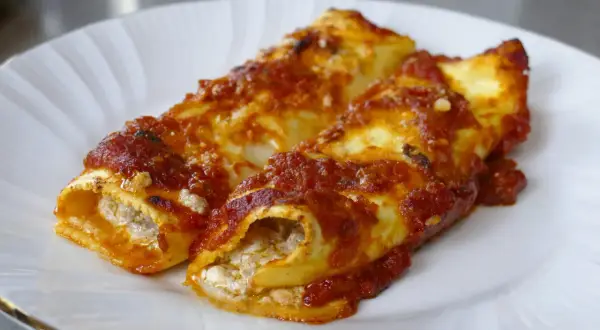 Due cannelloni di carne ripieni e ricoperti di sugo rosso, serviti su un piatto bianco.