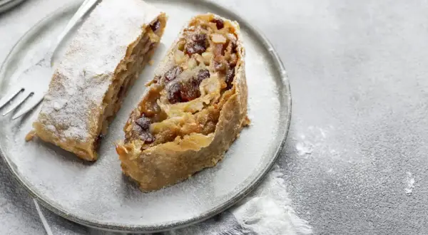 Due fette di strudel di mele su un piatto, cosparse di zucchero a velo. Un dolce invitante pronto da gustare.
