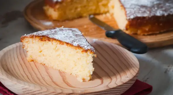 Una fetta di torta all'acqua soffice e spolverata di zucchero a velo su un piatto di legno.