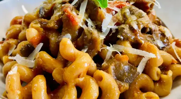 Un piatto invitante di pasta con melanzane, condita con un ricco sugo e scaglie di parmigiano.