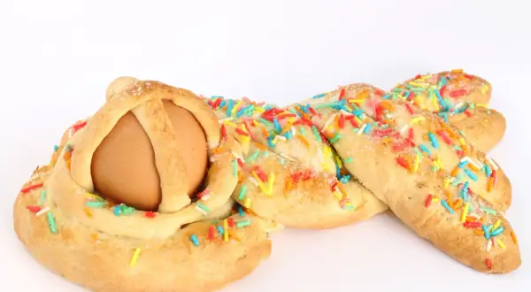 Una cuzzupa intrecciata con un uovo al centro, decorata con zuccherini colorati.