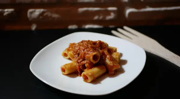 Piatto di pasta alla portofino con sugo rosso e forchetta in legno sullo sfondo di mattoni.