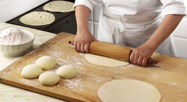Mani esperte stendono la pasta per una piadina fatta in casa, mentre altre sono già pronte per essere cotte.