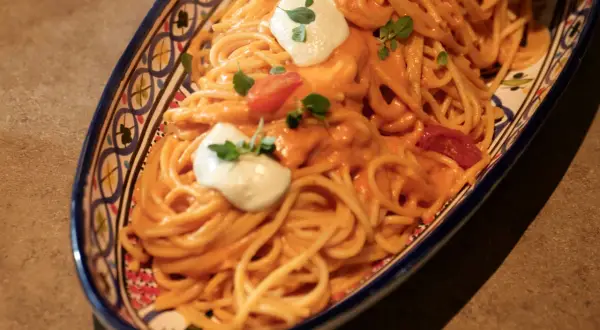 Un invitante piatto di pasta con pomodorini, condita con una cremosa salsa e guarnita con ricotta fresca e basilico.