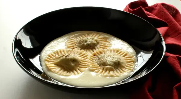 Tre ravioli di borragine, con un ripieno cremoso e una spolverata di pepe, serviti in una ciotola nera su un tovagliolo rosso.