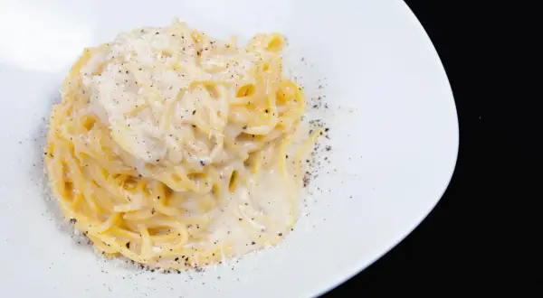 Pici cacio e pepe, un classico piatto di pasta romana, servito su un piatto bianco con abbondante pepe nero macinato e formaggio grattugiato.