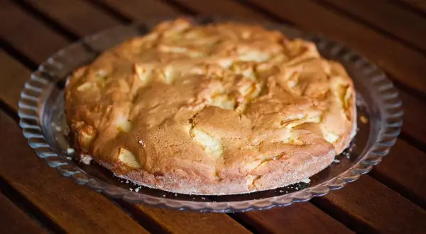 Torta di pane e mele alla trentina, dorata e invitante, su un piatto di vetro, pronta per essere gustata.