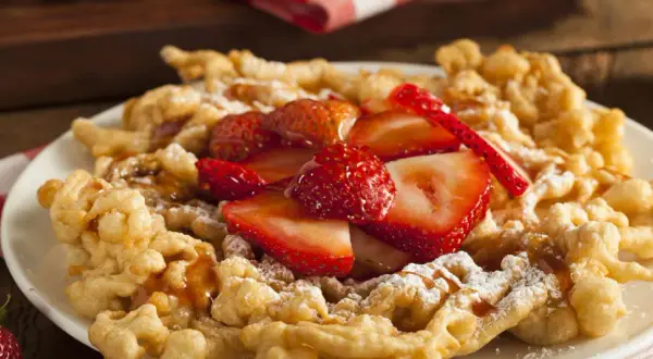 Strauben croccanti, guarniti con fragole fresche e zucchero a velo. Una deliziosa ricetta per un dolce da fiera.