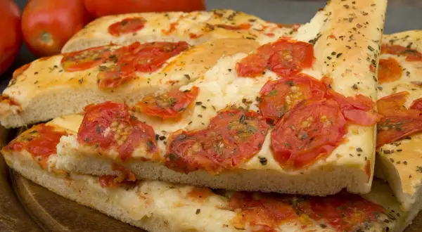 Focaccia barese soffice e dorata, condita con pomodorini freschi e origano, pronta per essere gustata.