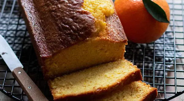 Plumcake all'arancia appena sfornato, dorato e profumato, con fette morbide e arance fresche accanto.